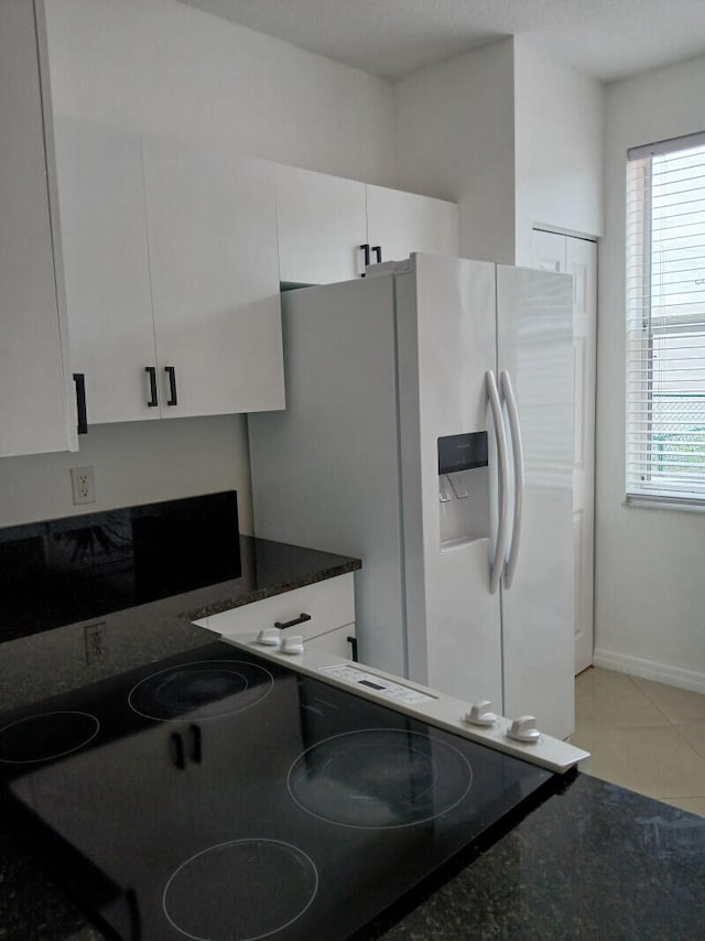 kitchen with dark stone countertops, white refrigerator with ice dispenser, white cabinetry, electric cooktop, and light tile patterned floors