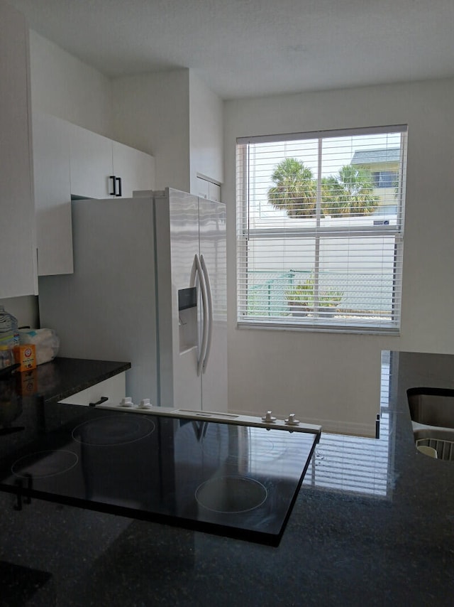 kitchen with refrigerator with ice dispenser, black electric stovetop, and white cabinetry