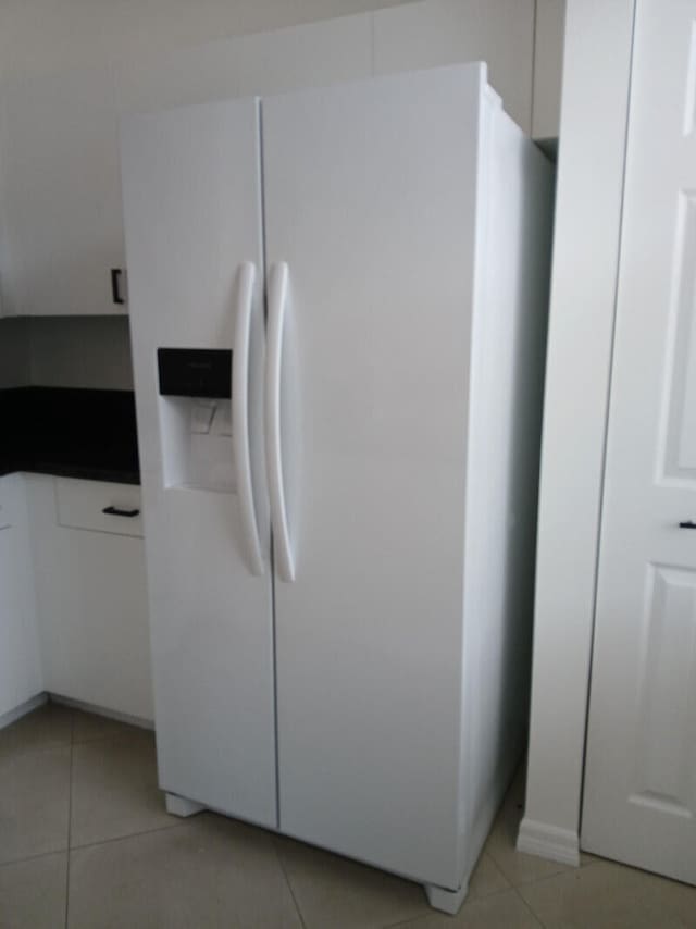 interior space with white cabinets, light tile patterned floors, and white fridge with ice dispenser