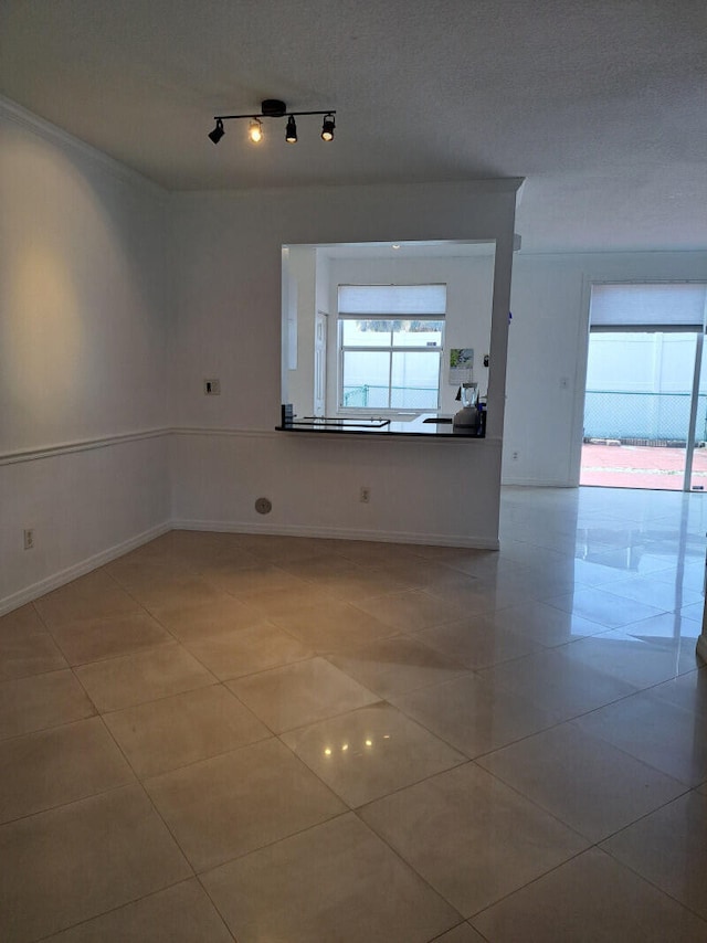 empty room featuring track lighting, a textured ceiling, and tile patterned flooring