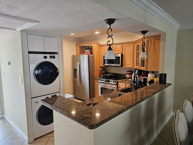 kitchen featuring dark stone countertops, light tile patterned floors, decorative light fixtures, stainless steel appliances, and stacked washing maching and dryer