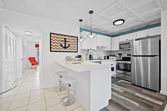 kitchen featuring a peninsula, an ornate ceiling, stainless steel appliances, light countertops, and tasteful backsplash