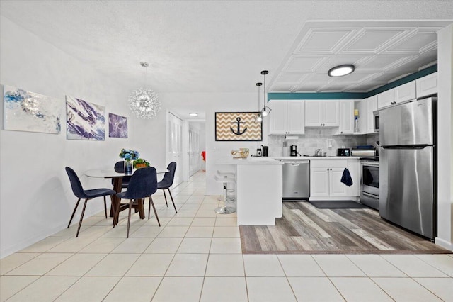 kitchen with hanging light fixtures, light tile patterned floors, appliances with stainless steel finishes, decorative backsplash, and white cabinets