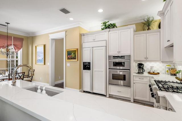 kitchen featuring visible vents, decorative light fixtures, ornamental molding, stainless steel appliances, and a sink