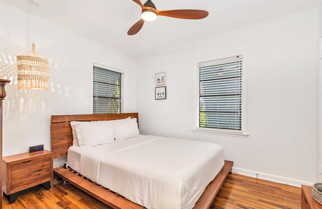 bedroom with ceiling fan with notable chandelier and hardwood / wood-style floors