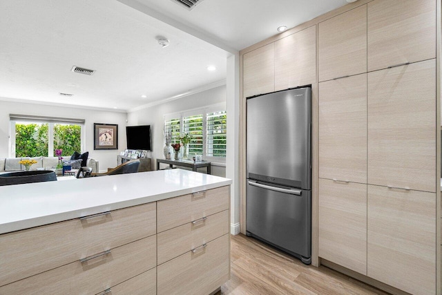 kitchen featuring light wood-type flooring, stainless steel fridge, ornamental molding, and light brown cabinets