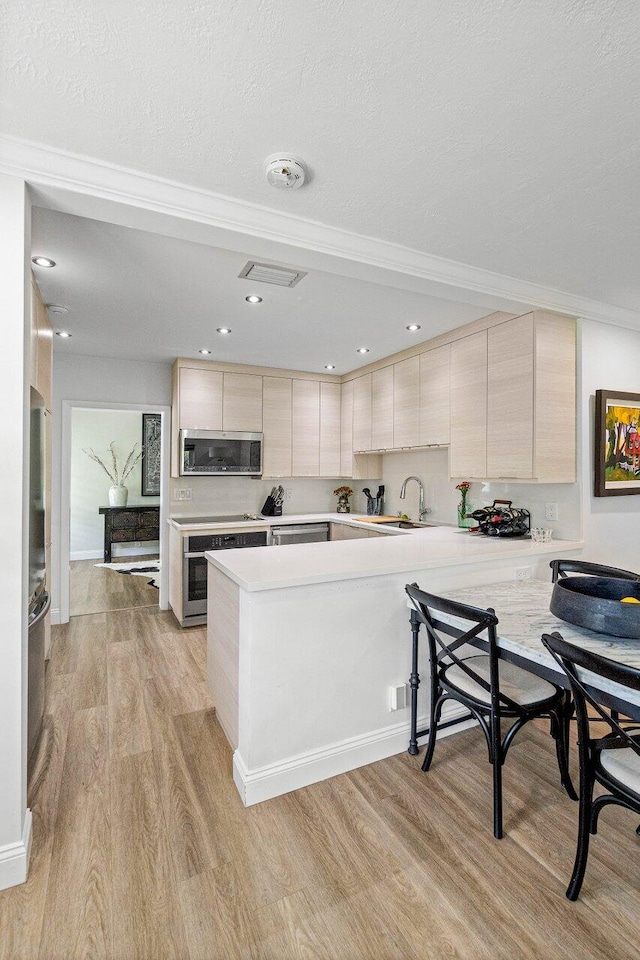 kitchen with light wood-type flooring, stainless steel appliances, sink, kitchen peninsula, and a kitchen bar