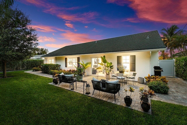 back house at dusk featuring a patio area and a yard