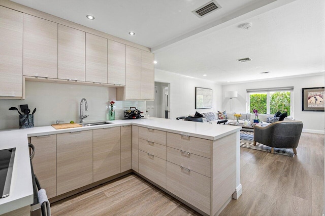 kitchen with light wood-type flooring, light brown cabinetry, kitchen peninsula, and sink