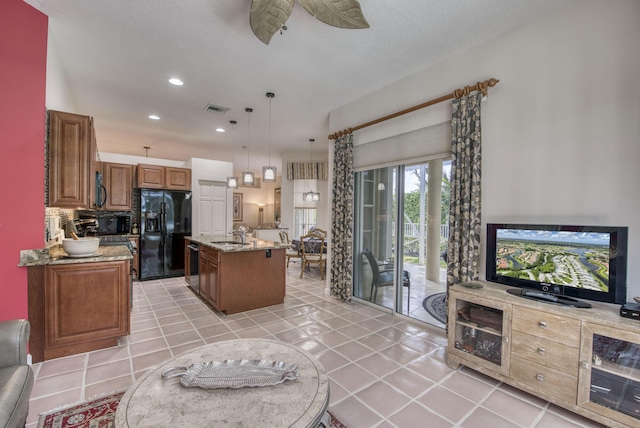 kitchen featuring visible vents, brown cabinetry, decorative light fixtures, a kitchen island with sink, and black appliances