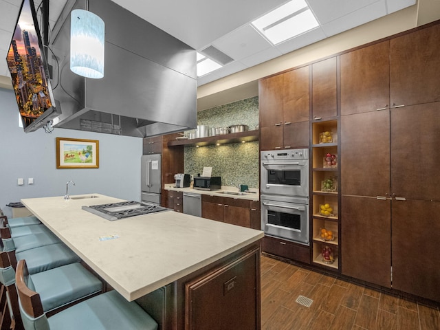 kitchen featuring dark wood-type flooring, stainless steel appliances, a breakfast bar area, and decorative light fixtures