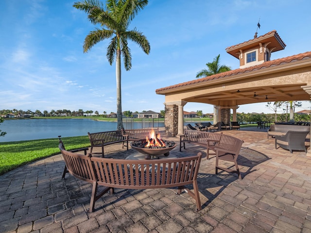 view of patio featuring a gazebo, ceiling fan, an outdoor living space with a fire pit, and a water view