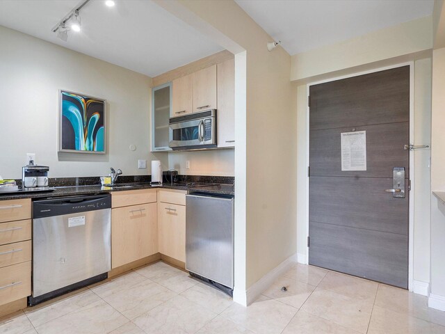 kitchen featuring stainless steel appliances, dark stone countertops, light brown cabinetry, and sink