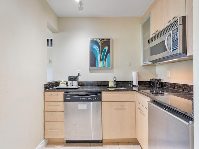 kitchen with dark stone countertops, light brown cabinetry, sink, and stainless steel appliances