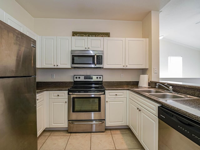 kitchen featuring appliances with stainless steel finishes, vaulted ceiling, sink, light tile patterned floors, and white cabinets