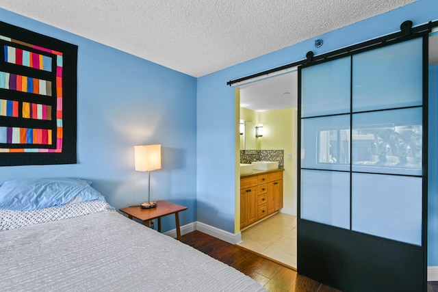 bedroom featuring a textured ceiling, wood-type flooring, ensuite bathroom, and a barn door