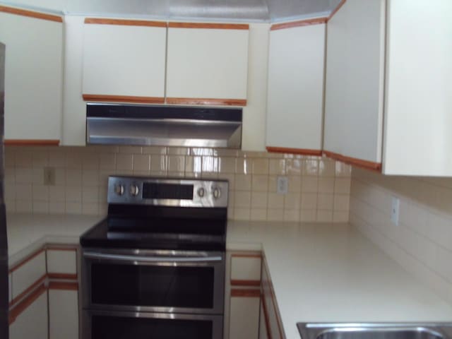 kitchen with stainless steel electric range, decorative backsplash, and white cabinets