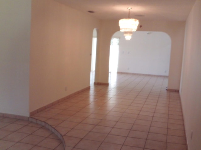 tiled empty room with an inviting chandelier