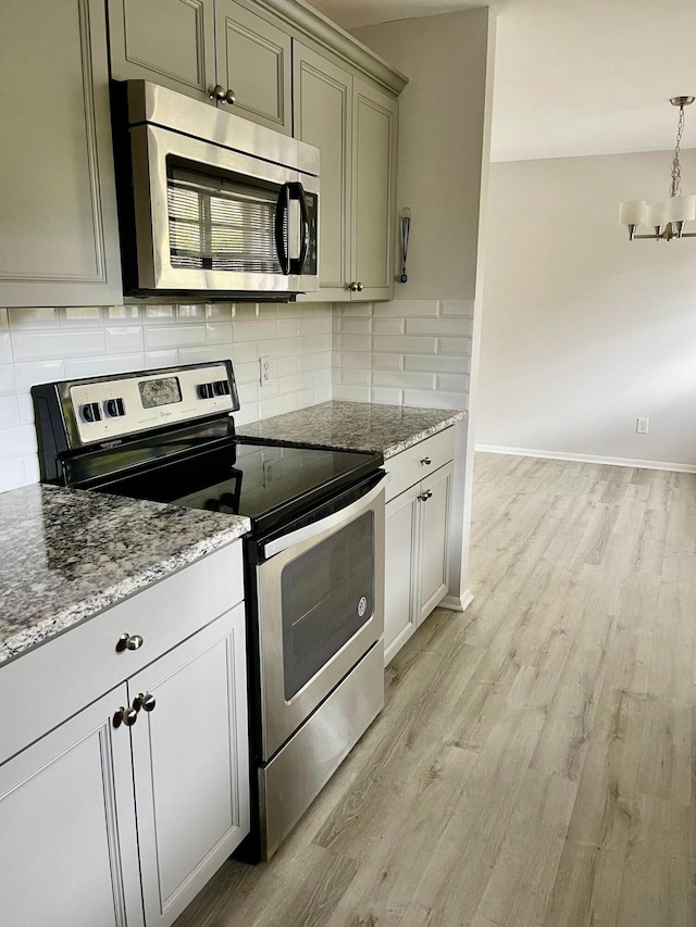 kitchen with appliances with stainless steel finishes, light stone counters, light hardwood / wood-style flooring, and backsplash