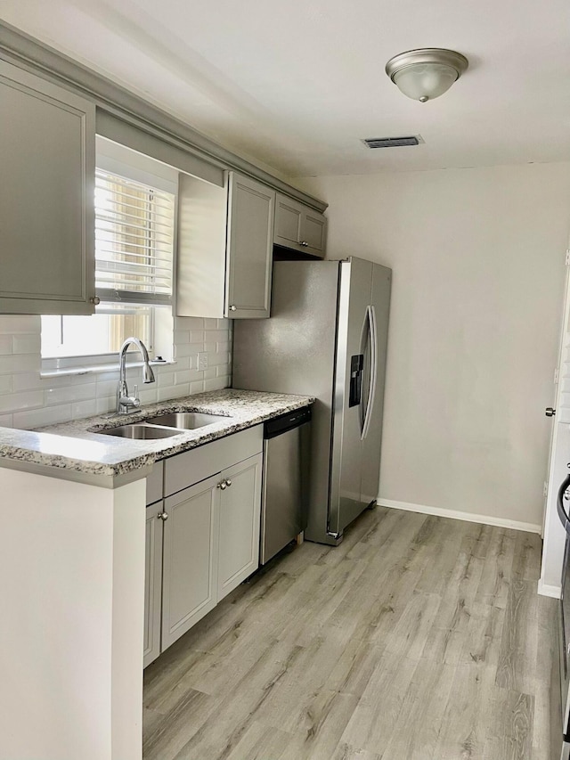 kitchen featuring stainless steel dishwasher, backsplash, sink, and light wood-type flooring