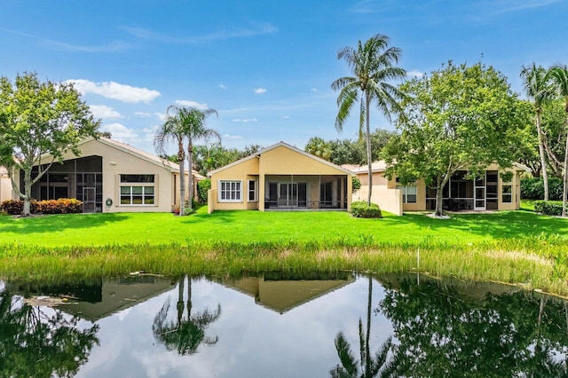 rear view of property featuring a sunroom, a lawn, and a water view