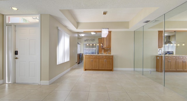 kitchen with pendant lighting, a tray ceiling, a wealth of natural light, and wall chimney range hood