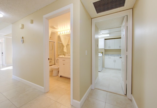 hall featuring washer / clothes dryer, light tile patterned flooring, and a textured ceiling