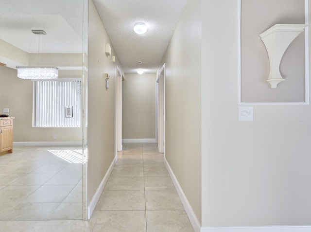 corridor featuring light tile patterned floors, a chandelier, and a textured ceiling