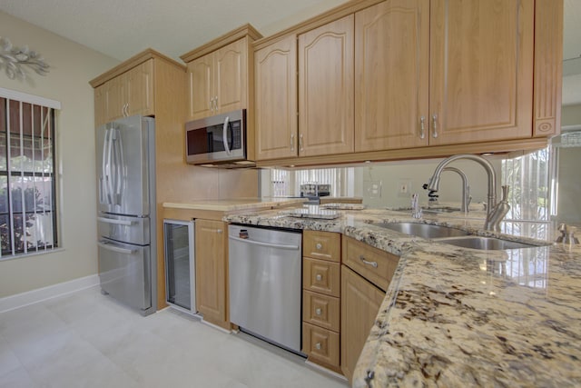 kitchen featuring appliances with stainless steel finishes, light brown cabinetry, light stone counters, sink, and wine cooler