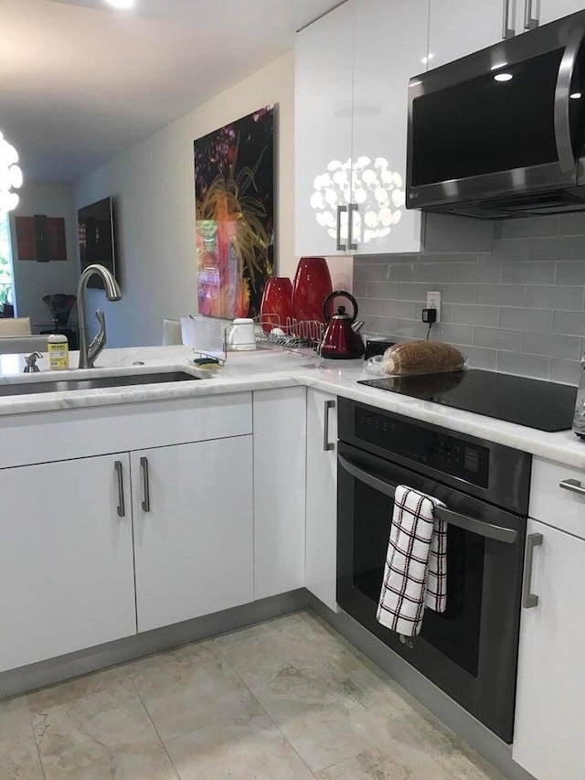 kitchen with white cabinets, backsplash, an inviting chandelier, appliances with stainless steel finishes, and sink