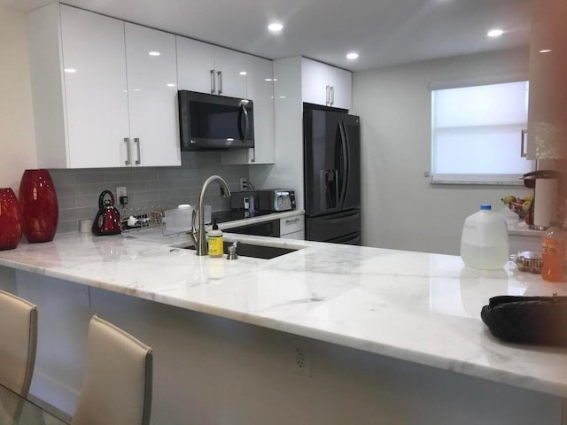 kitchen featuring black appliances, light stone countertops, backsplash, and white cabinets