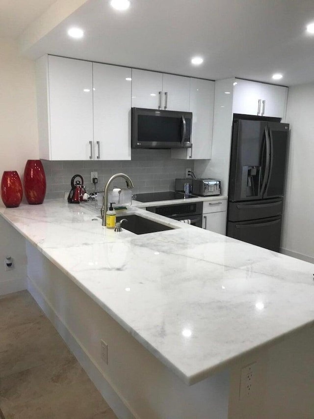 kitchen featuring kitchen peninsula, sink, decorative backsplash, black fridge, and white cabinets