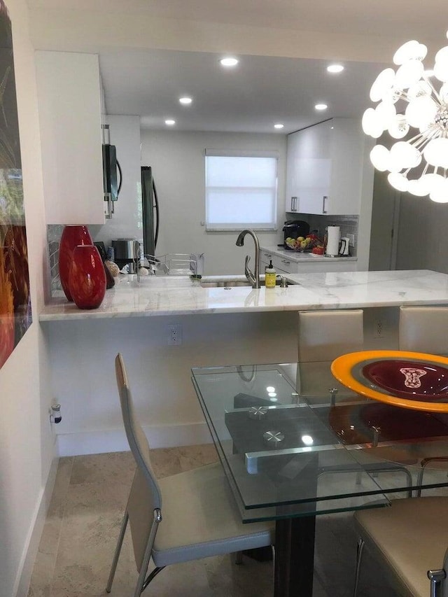 kitchen with black appliances, kitchen peninsula, sink, white cabinetry, and light tile patterned flooring