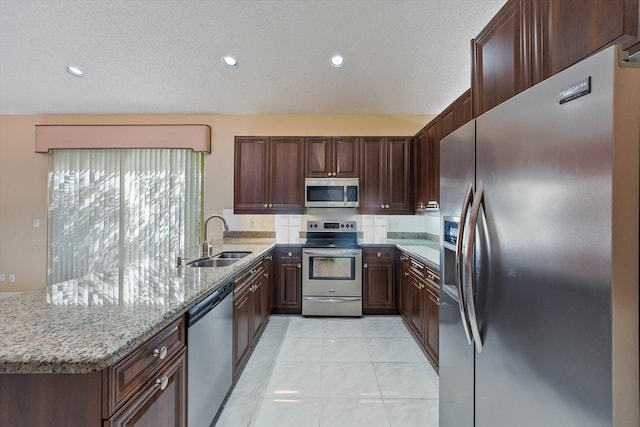 kitchen with light stone countertops, a textured ceiling, stainless steel appliances, and sink