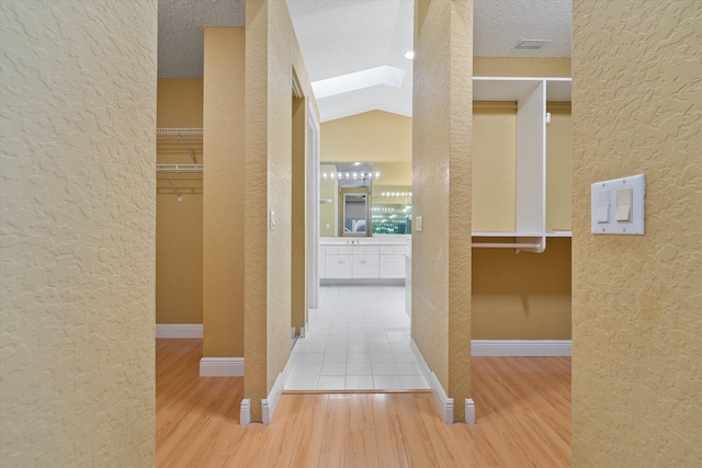 hallway with lofted ceiling with skylight, a textured ceiling, and hardwood / wood-style floors