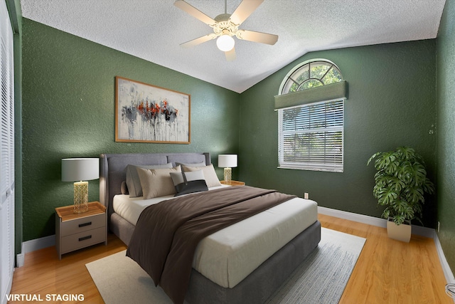 bedroom featuring lofted ceiling, light hardwood / wood-style floors, ceiling fan, and a textured ceiling