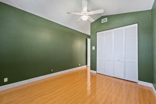 unfurnished bedroom featuring vaulted ceiling, a closet, a textured ceiling, ceiling fan, and hardwood / wood-style floors