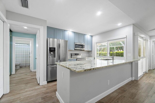 kitchen with light hardwood / wood-style flooring, light stone countertops, stainless steel appliances, and sink