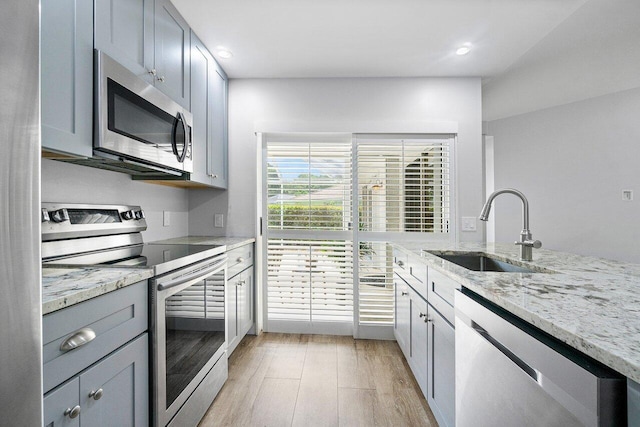 kitchen with gray cabinetry, a sink, light stone counters, stainless steel appliances, and light wood-style floors