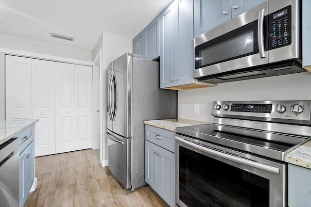 kitchen with appliances with stainless steel finishes, light stone countertops, and light hardwood / wood-style flooring