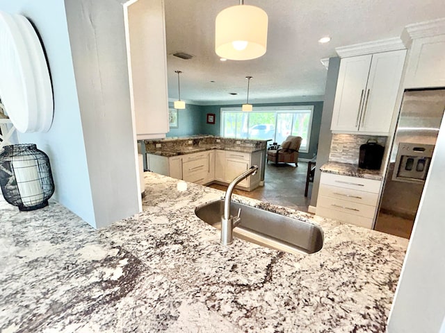 kitchen featuring decorative light fixtures, light stone countertops, kitchen peninsula, sink, and white cabinetry