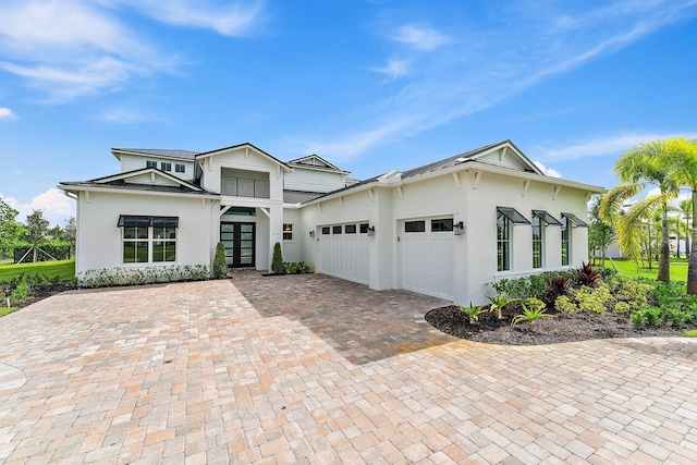 view of front facade with an attached garage, stucco siding, a standing seam roof, decorative driveway, and french doors