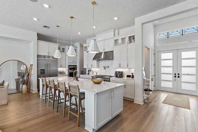 kitchen with a breakfast bar area, a center island with sink, wood-type flooring, hanging light fixtures, and white cabinetry