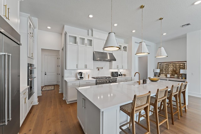 kitchen with light wood-type flooring, an island with sink, white cabinetry, and sink