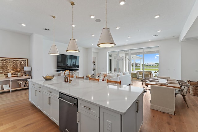 kitchen featuring white cabinetry, dishwasher, light stone counters, a center island with sink, and light hardwood / wood-style floors