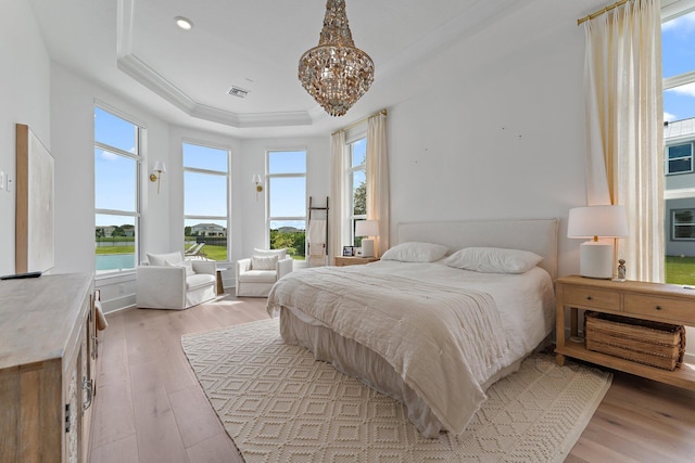 bedroom featuring light wood-style floors, a raised ceiling, a chandelier, and visible vents