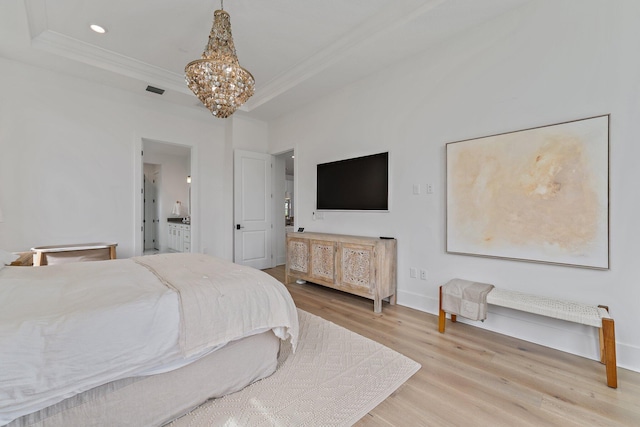 bedroom featuring an inviting chandelier, light hardwood / wood-style floors, a raised ceiling, and ensuite bathroom