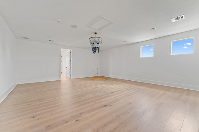 empty room with baseboards, attic access, light wood finished floors, and visible vents