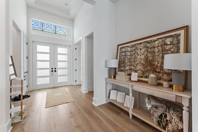foyer with french doors, baseboards, a towering ceiling, and wood finished floors