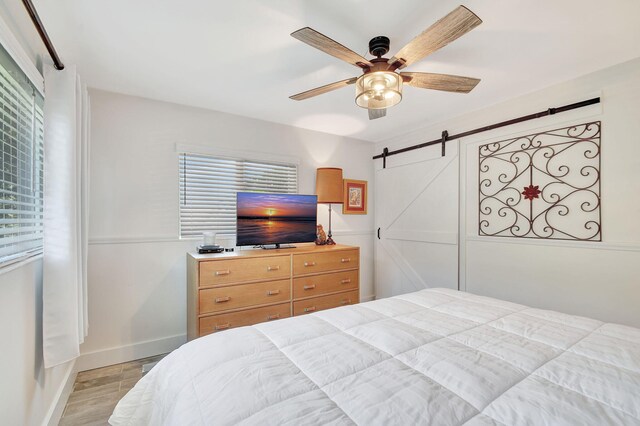 bedroom featuring baseboards, a barn door, a ceiling fan, and light wood-style floors